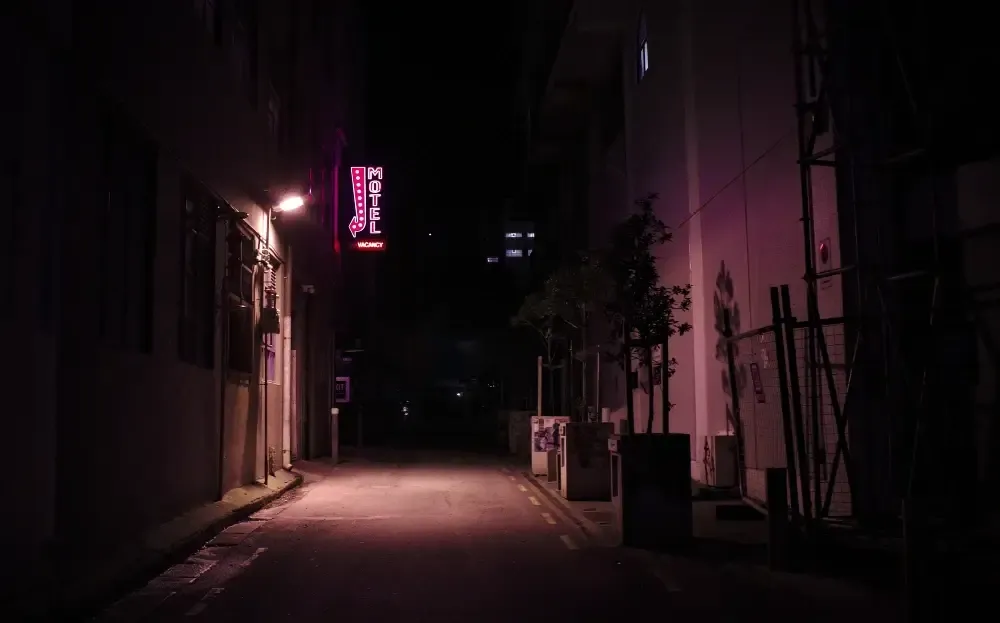 Dimly lit street at night featuring a motel sign and shadows from nearby buildings.